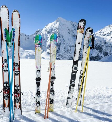 3 pairs of skis and poles standing upright in snow at side of piste on sunny day